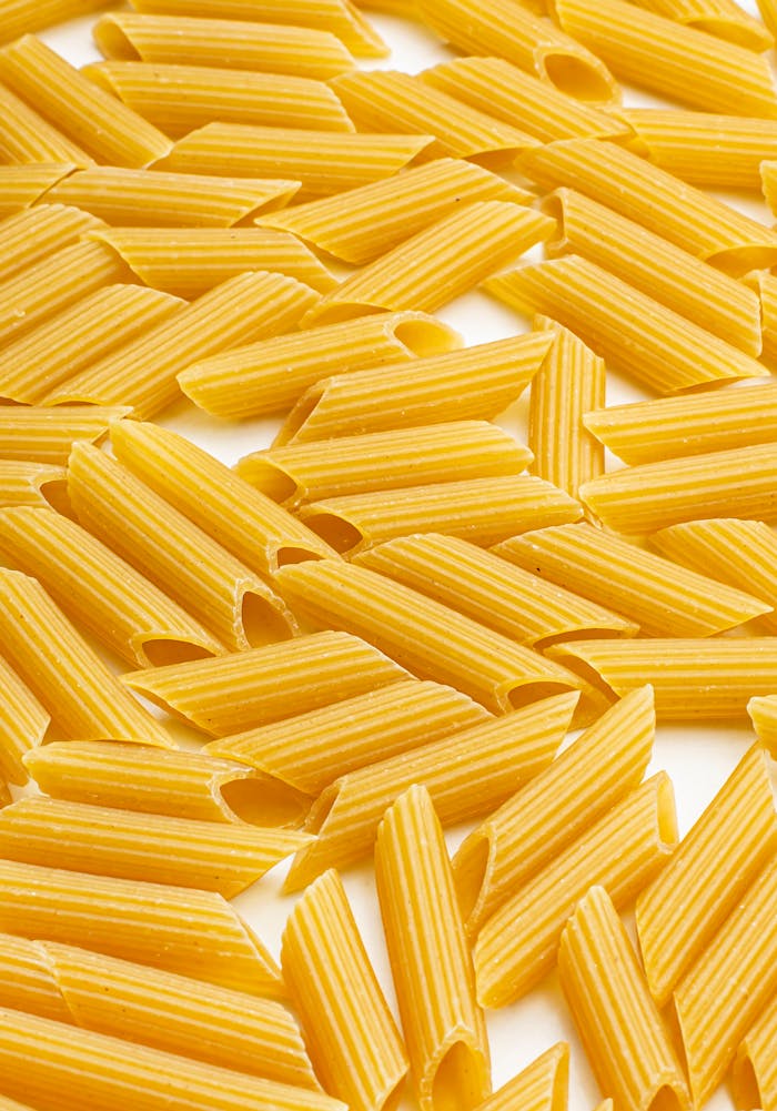 High-resolution close-up of raw penne pasta scattered on a white surface, perfect for Italian cuisine themes.